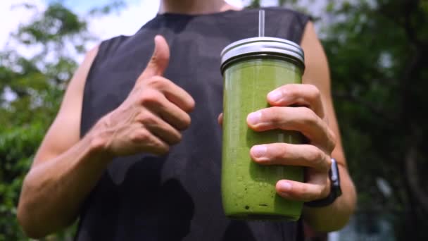 Sportler zeigt Daumen hoch und hält gesunden grünen Smoothie in der Hand. Nahaufnahme. — Stockvideo