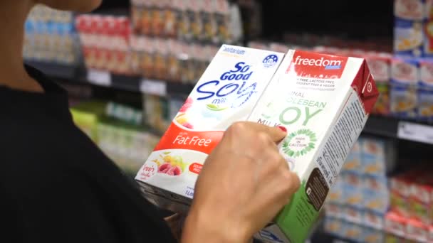 Manos de cliente hembra sosteniendo leche de soja mientras compra en el supermercado. BANGKOK, TAILANDIA - 16 DE ABRIL DE 2018 . — Vídeo de stock