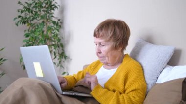 Büyükannem dizüstü bilgisayar kullanıyor. Yatakta dinleniyor. Yaşlılara Bakım, Teknoloji Konsepti.
