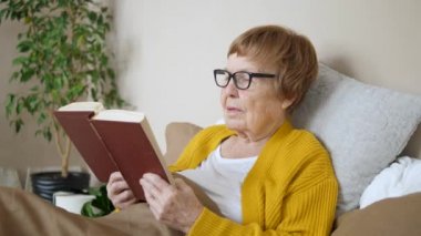 Evde yatağında kitap okuyan yaşlı bir kadın.