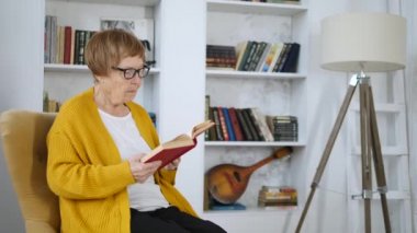 Yaşlı kadın evde kitap okuyor.