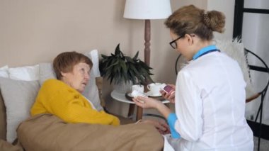 Doktor, yaşlı kadına ilaç yazarken elinde haplarla şişe tutuyor..