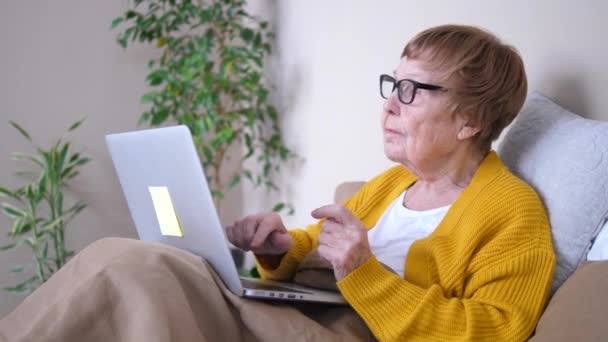 Бабушка использует ноутбук компьютер релаксации в постели. Вычислительные услуги для пенсионеров . — стоковое видео