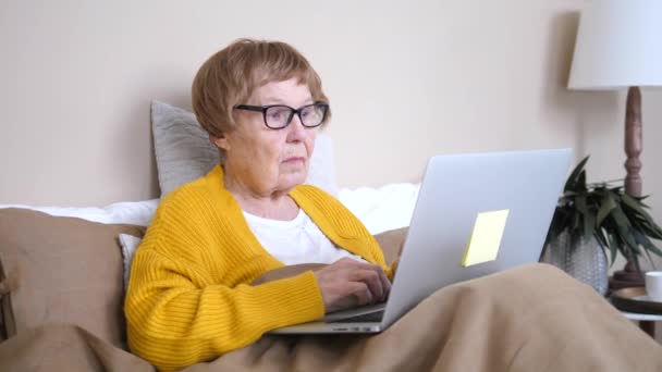 Усталая пожилая женщина страдает от головной боли после использования ноутбука дома — стоковое видео