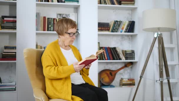 Бабуся розслабляється вдома читаючи книгу — стокове відео