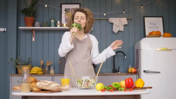 Joven mujer feliz cantando y bailando en la cocina mientras cocina comida saludable . — Vídeos de Stock