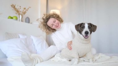 Evde köpeğiyle yatakta oturan gülümseyen genç kadın..