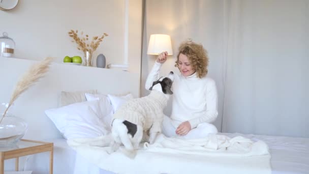 Молодая женщина играет с собакой на кровати в спальне — стоковое видео