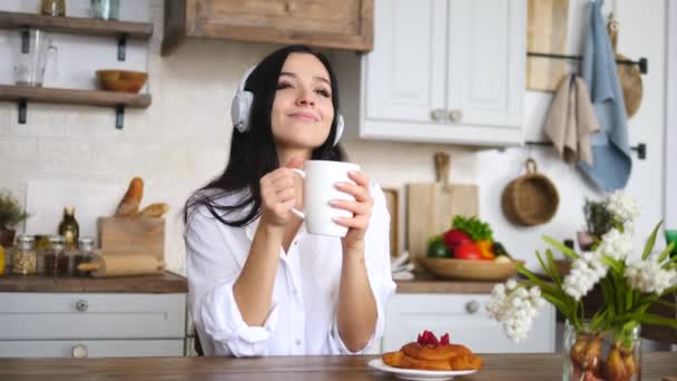 Молода жінка слухає музику з навушниками вдома з кавою — стокове відео