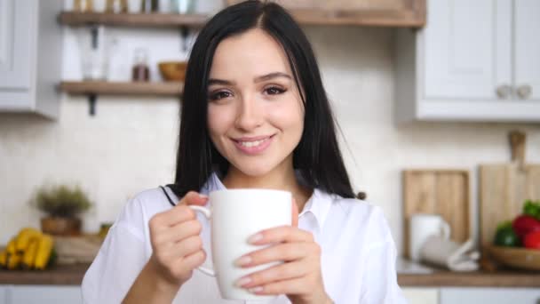 Portrait de attrayant Brunette femelle regardant caméra tenant tasse dans la cuisine — Video