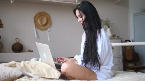 Νεαρή γυναίκα που χρησιμοποιεί φορητό υπολογιστή στο κρεβάτι στο σπίτι — Αρχείο Βίντεο