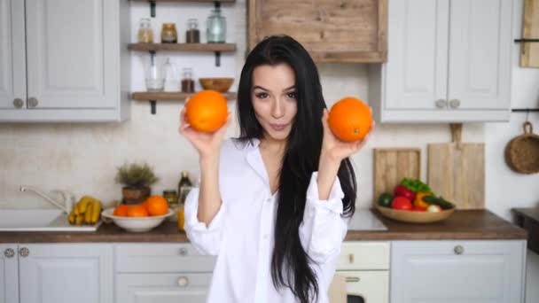 Πορτρέτο της νεαρής αστείας γυναίκας που χορεύει με πορτοκαλί πάνω από τα μάτια στην κουζίνα. Διατροφή και υγιεινή διατροφή έννοια. — Αρχείο Βίντεο