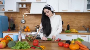 Esmer kadın mutfakta sağlıklı yemekler pişiriyor ve kulaklıkla dans ediyor.