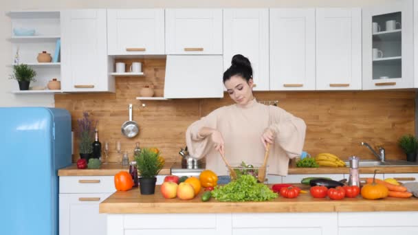 Jovem feliz prepara comida saudável na cozinha misturando salada — Vídeo de Stock