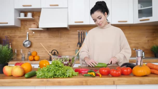 キッチンで新鮮な野菜のサラダを切る幸せな若い女性. — ストック動画
