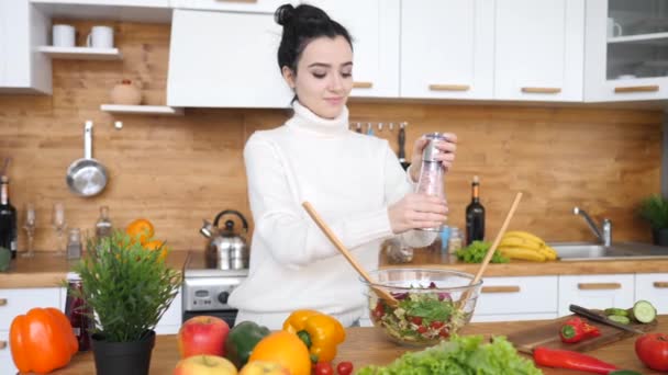 Junge Frau gibt Salz in die Schüssel, während sie Salat in der Küche kocht. — Stockvideo