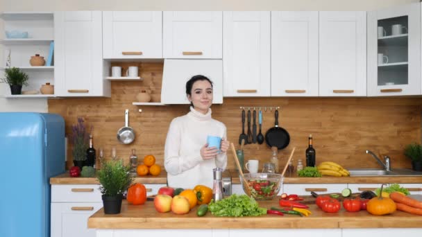 Retrato de una mujer joven sosteniendo una taza de café en la cocina . — Vídeos de Stock