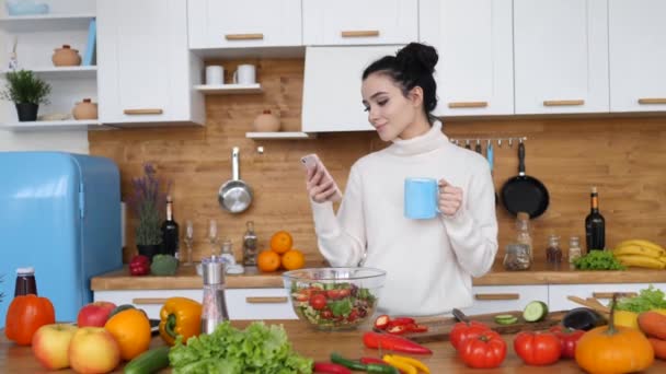 Jovem mulher usando Smartphone e sorrindo na cozinha — Vídeo de Stock