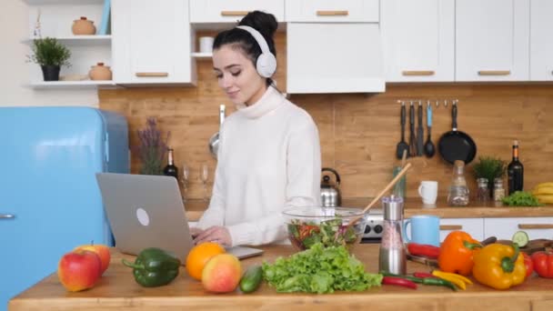 Jeune femme utilisant un ordinateur portable tout en cuisinant dans la cuisine — Video