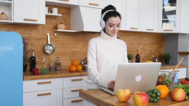 在厨房做饭时使用笔记本电脑的年轻女人. — 图库视频影像