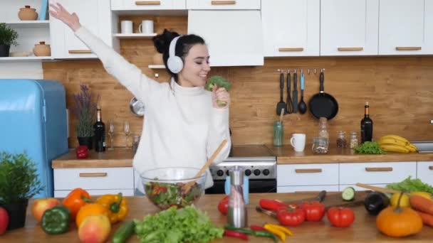 Joven chica alegre cantando en brócoli bailando en la cocina mientras cocina la cena . — Vídeo de stock