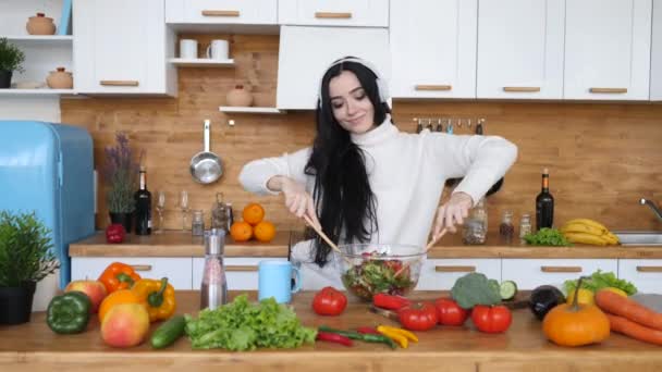 Jeune femme cuisine salade végétalienne saine à la maison en écoutant de la musique dans les écouteurs — Video