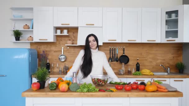 Hermosa joven cocina en la cocina y sonriendo en la cámara — Vídeos de Stock