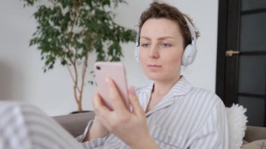 Genç bayan evde dinleniyor, akıllı telefondan müzik dinliyor ve kulaklık takıyor.