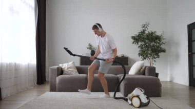 Adam evde elektrikli süpürgeyle sanal gitar çalıyor kulaklık takıp dans ediyor.