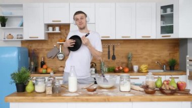Genç ve yakışıklı adam mutfakta yemek pişirirken kulaklıkla tavayla oynuyor..