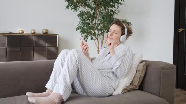Молода жінка використовує смартфон розслабляючись на дивані у вітальні — стокове відео