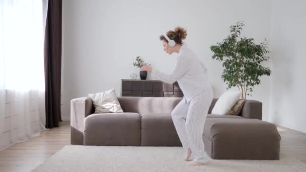 Jeune femme dansant avec Smartphone à la maison portant un pyjama et un casque . — Video