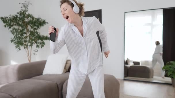Mujer joven feliz en los auriculares escuchando música con el teléfono inteligente, bailando y sonriendo — Vídeo de stock