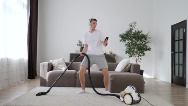Mladý muž baví čištění domu s vysavač tanec a použití Smartphone. — Stock video