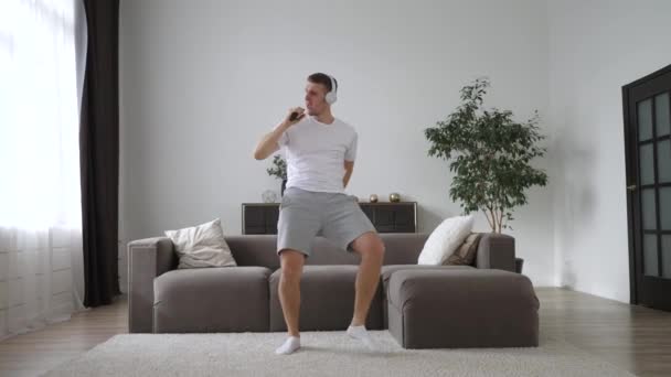 Веселый мужчина поет и танцует с телефоном дома — стоковое видео