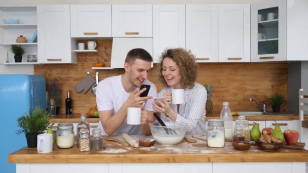 Nettes fröhliches Paar nutzt Smartphone zu Hause in der Küche — Stockvideo
