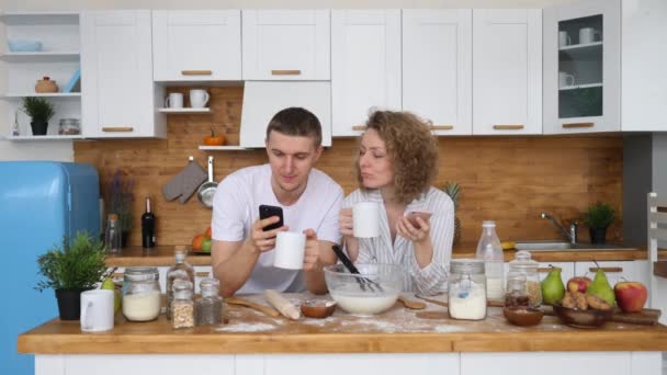 Casal feliz usando telefones celulares na cozinha. Conceito de Pessoas e Tecnologia . — Vídeo de Stock