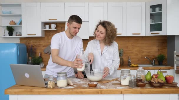 Joven pareja feliz preparación de alimentos en la cocina y lectura receta en el ordenador portátil . — Vídeos de Stock