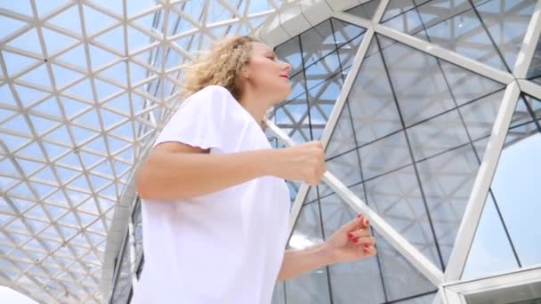 Jonge gelukkige vrouw op de vlucht in de moderne stad. Langzame beweging. — Stockvideo