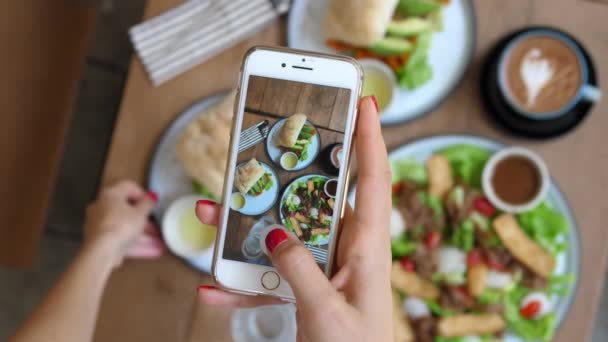 Manos femeninas con teléfono móvil tirando historias de comida en el almuerzo. Sandwich de aguacate . — Vídeos de Stock