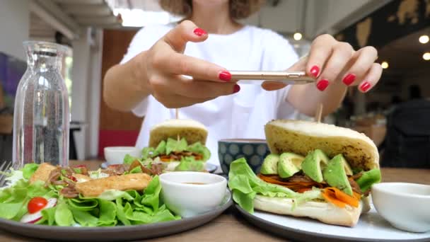 Egy nő fotózza az egészséges vegán avokádós szendvicset okostelefonnal az ebédnél — Stock videók
