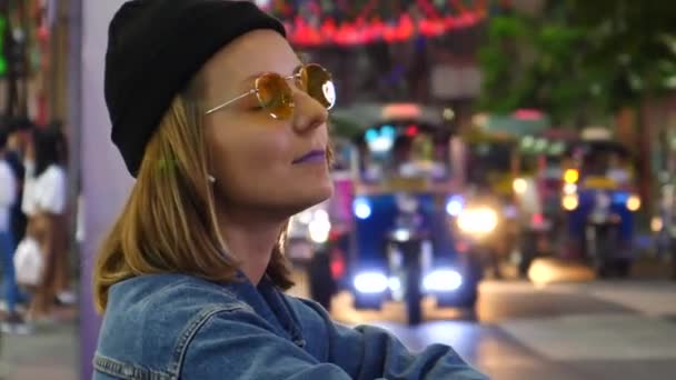 Mujer joven de moda en auriculares inalámbricos en la ciudad moderna por la noche — Vídeo de stock