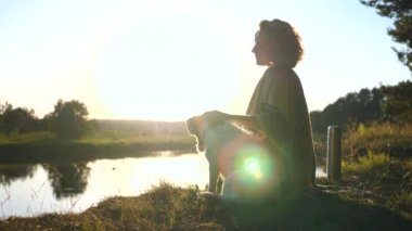 Genç kadın ve köpek Riverside 'da yaz günbatımının tadını çıkarıyorlar.