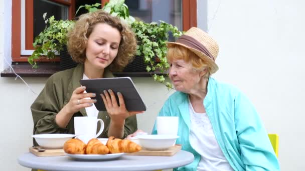 Внучка помогает бабушке с планшетом в кафе — стоковое видео
