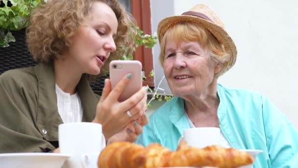 Внучка и бабушка используют смартфон в кафе — стоковое видео