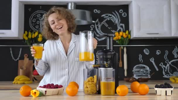 Mulher nova bonita na cozinha que espreme o suco de laranja com Juicer — Vídeo de Stock
