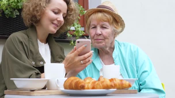 Petite-fille et grand-mère utilisant un smartphone ensemble au café — Video