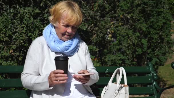 Farmor Dricka kaffe och använda smartphone utomhus — Stockvideo