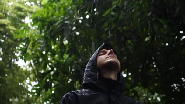 Glad bekymmerslös man inför himlen njuter av regnet bland gröna träd. — Stockvideo