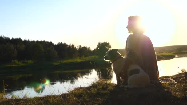 Frau und Hund sitzen bei Sonnenuntergang am Ufer des Flusses — Stockvideo